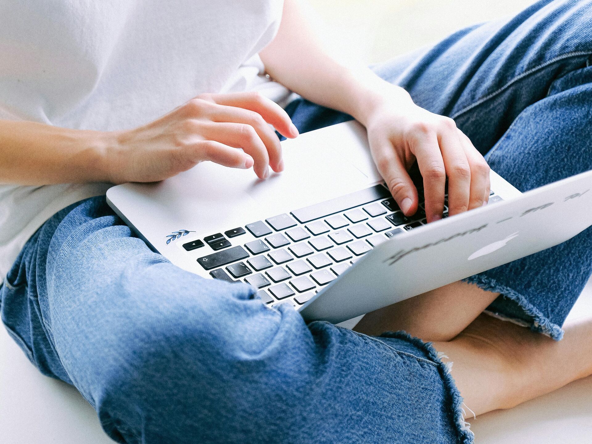 Person sitzt barfuß im Schneidersitz und arbeitet auf einem Laptop.