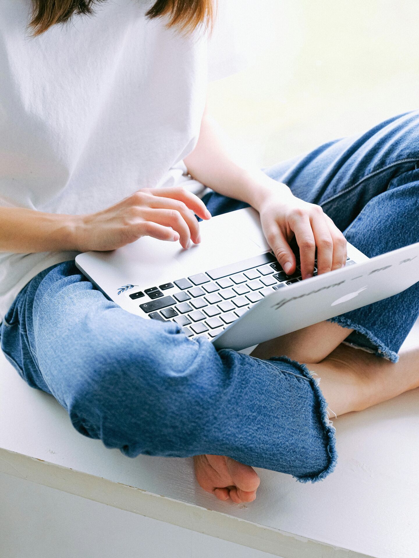 Person sitzt barfuß im Schneidersitz und arbeitet auf einem Laptop.