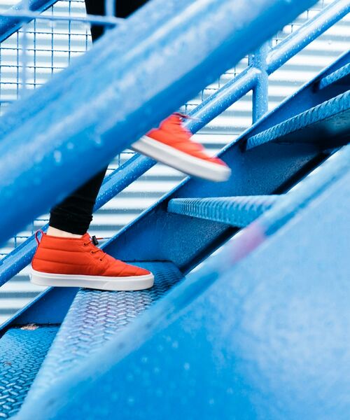 Person mit roten Sneakern steigt eine blaue Metalltreppe hinauf.