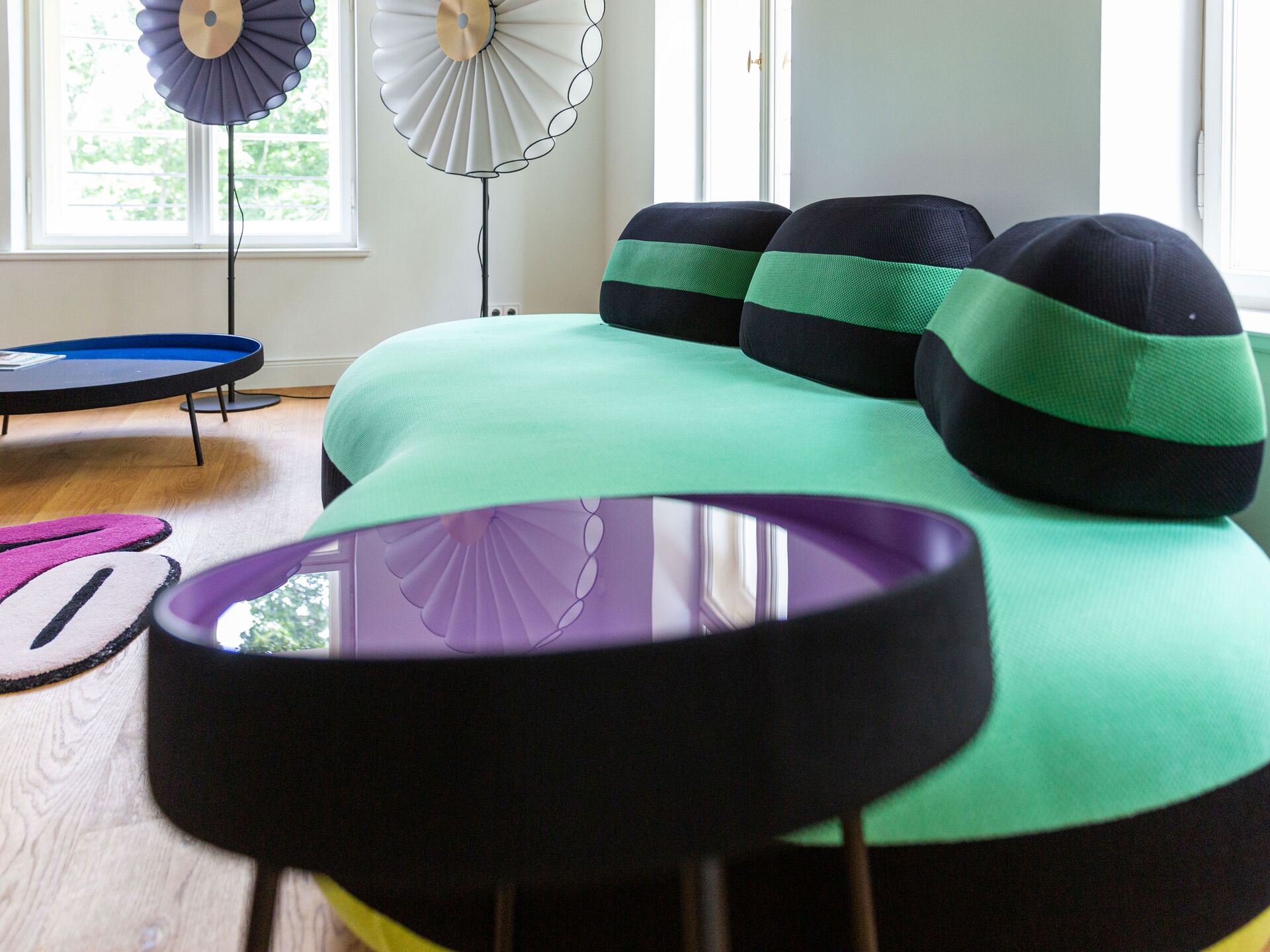 Modernes Wohnzimmer mit grün-schwarzem Designersofa und reflektierendem lilafarbenem Beistelltisch.