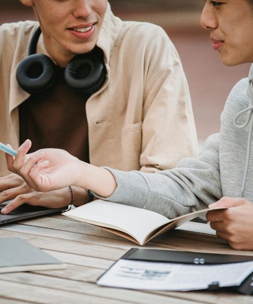 Zwei Personen sitzen gemeinsam am Tisch, sprechen miteinander und machen sich Notizen.