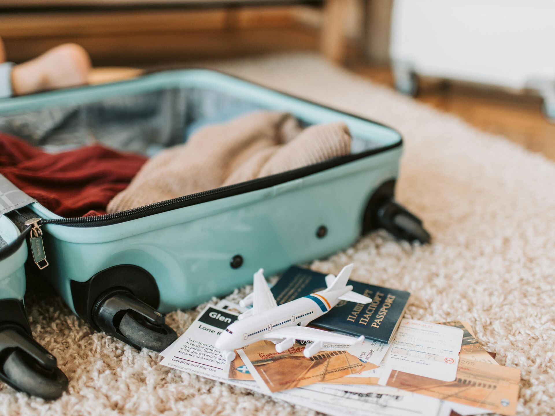 Offener Koffer mit Kleidung, daneben liegen Reisepass, Flugtickets und ein kleines Modellflugzeug.