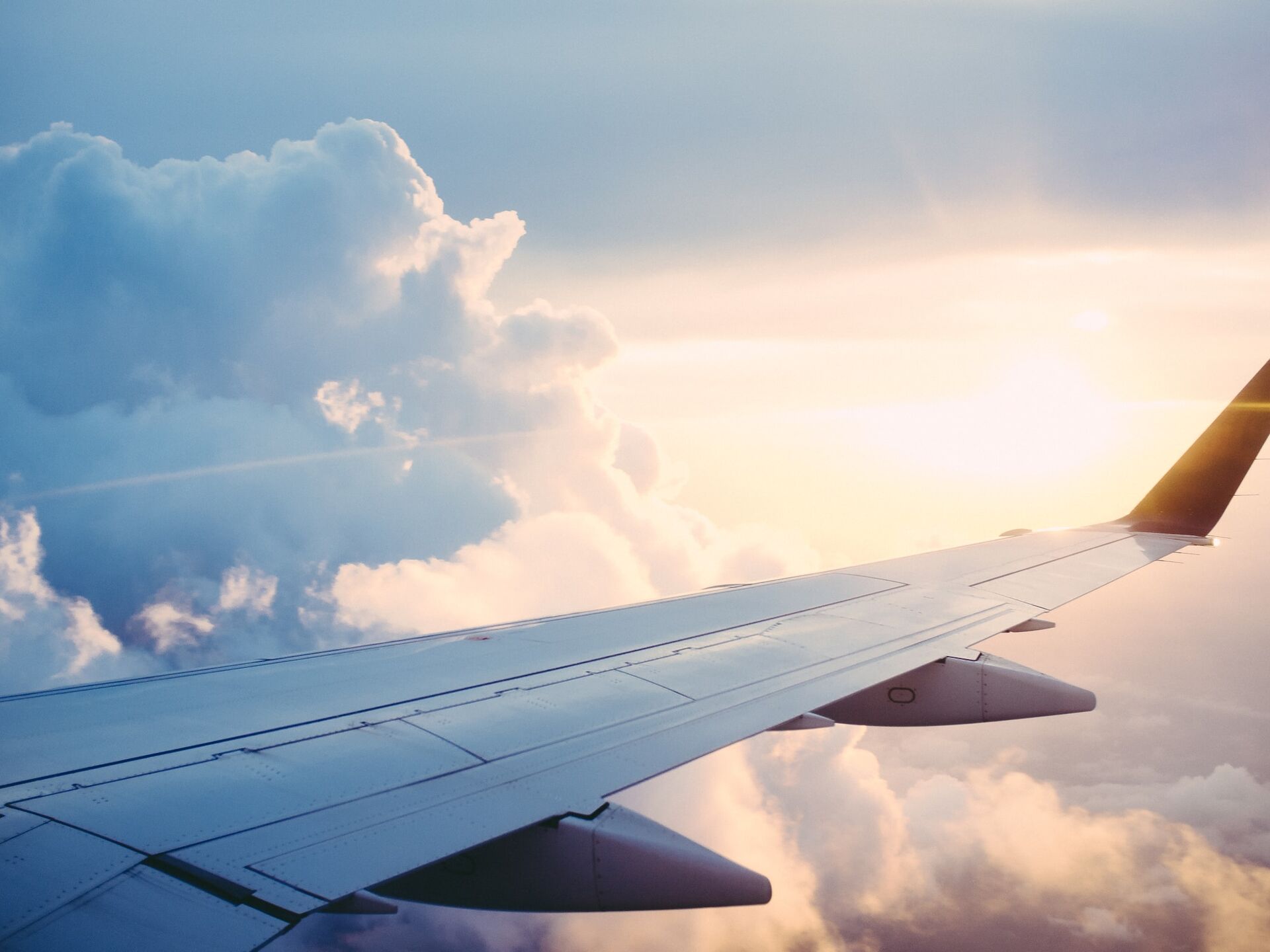 Blick aus dem Flugzeugfenster auf den Flügel über den Wolken bei Sonnenlicht, Symbol für Reisen und Aufbruch.