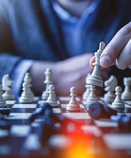 Hand setzt eine Schachfigur auf einem Schachbrett in strategischer Spielsituation.