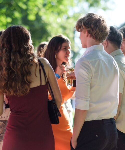 Gruppe junger Menschen unterhält sich bei einer Veranstaltung im Freien bei Sonnenschein.