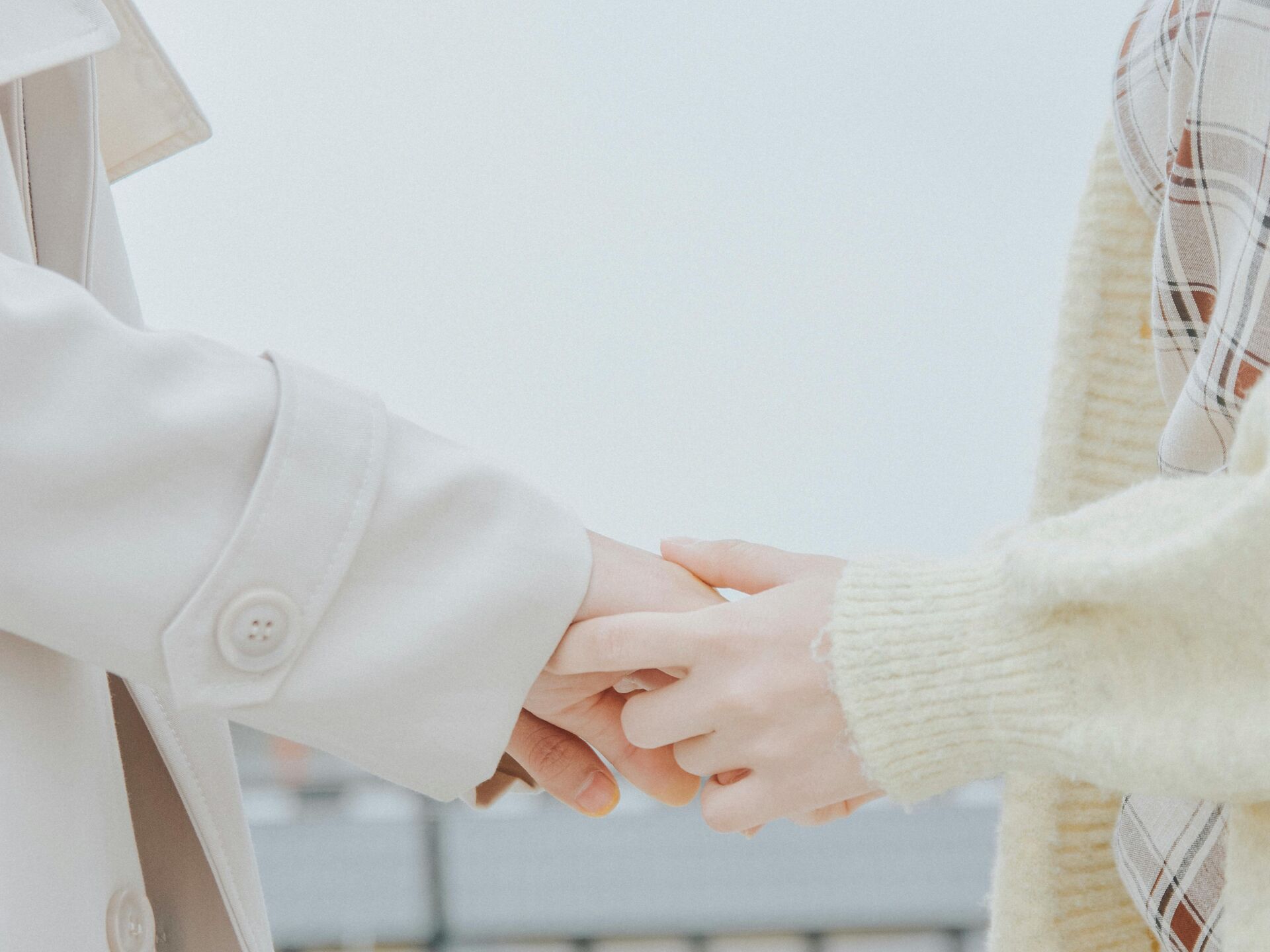 Zwei Personen halten sich sanft an den Händen, nur ihre Arme und Kleidung sind im Bild zu sehen.