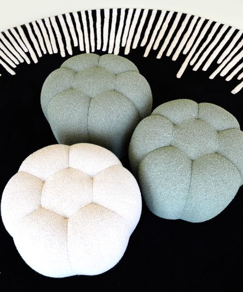 Drei runde, gepolsterte Hocker in Pastelltönen auf einem schwarzen Teppich mit weißem Muster.