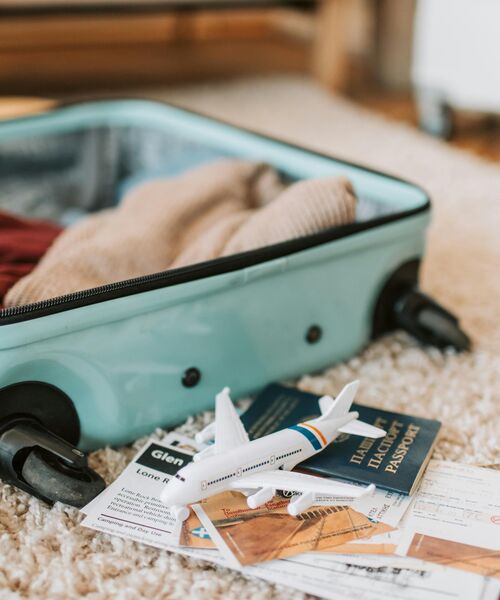 Offener Koffer mit Kleidung, daneben liegen Reisepass, Flugtickets und ein kleines Modellflugzeug.