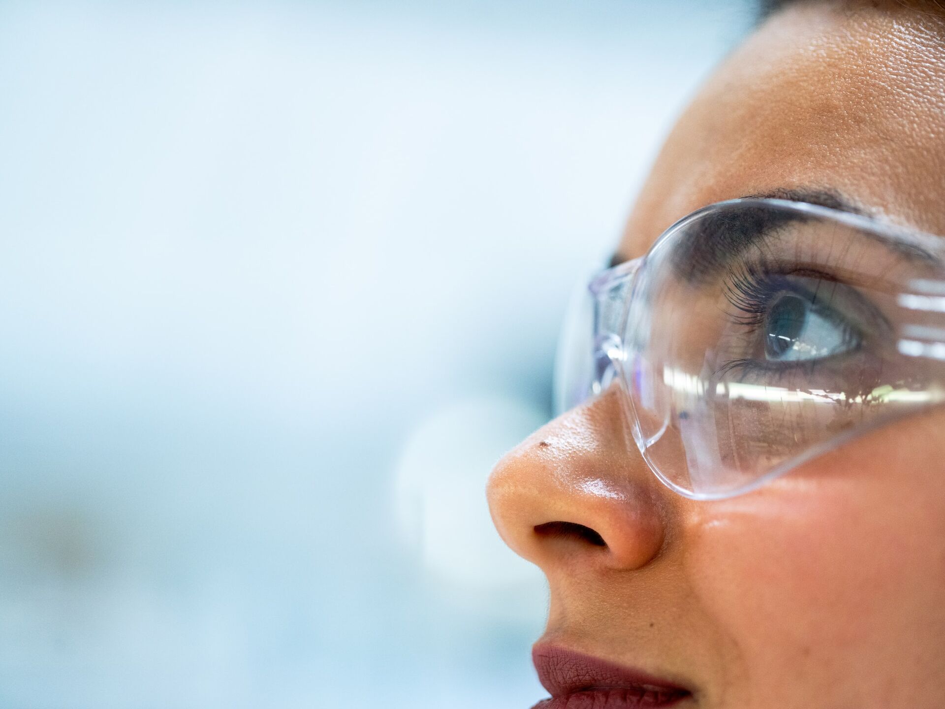 Nahaufnahme eines Gesichts mit Schutzbrille in einer hellen Laborumgebung.