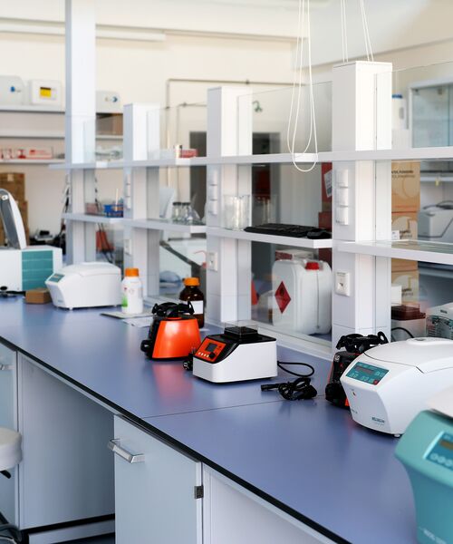 Laborarbeitsplatz mit verschiedenen Analysegeräten und Laborutensilien auf einer langen blauen Arbeitsfläche.